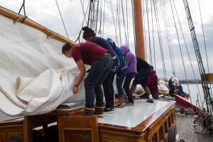 Crew members and Pathfinders help roll the sails as the boat prepares to return to port.