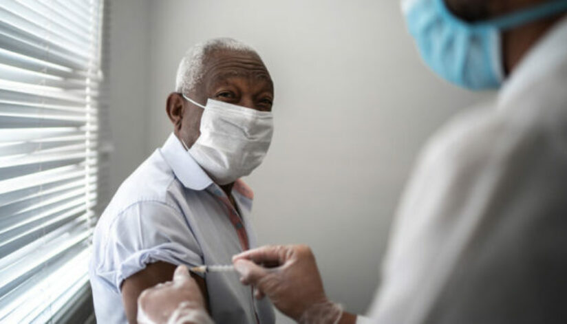 Nurse applying vaccine on patient's arm using face mask